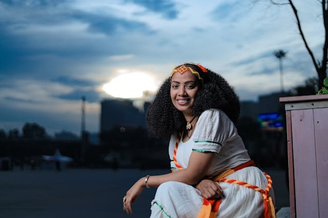 Smiling Woman with Curly Hair Sitting in Traditional Clothing